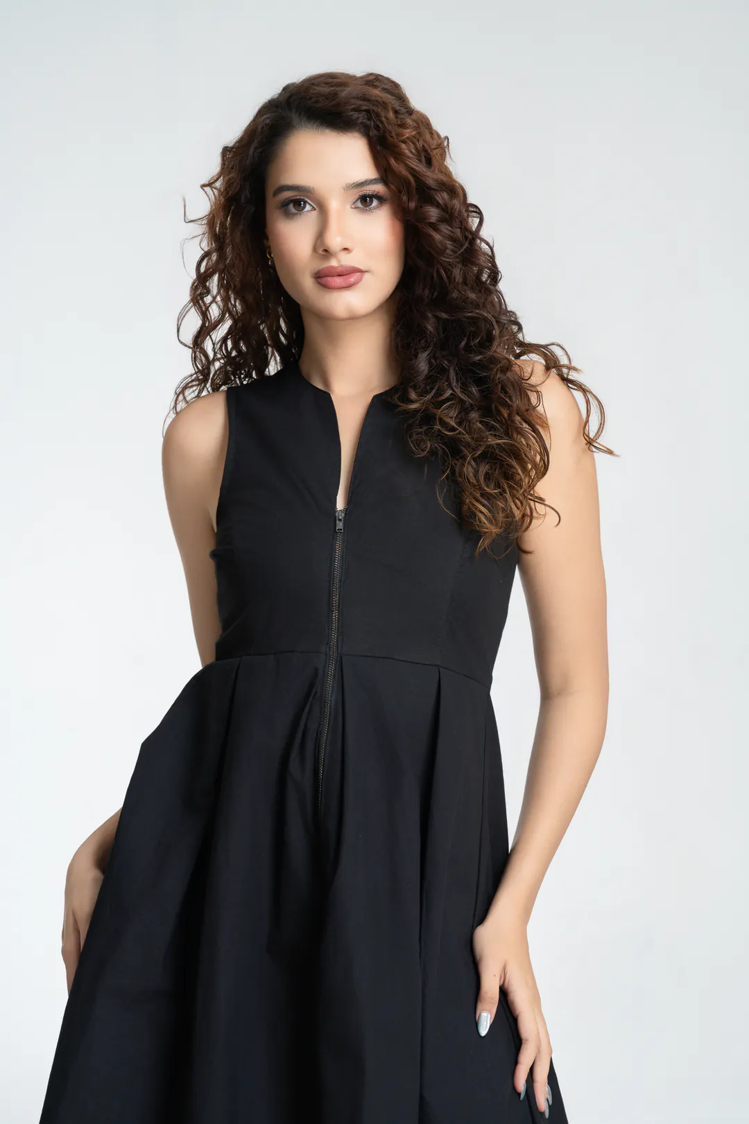 Model in a sleeveless black dress with a front zip and pleated skirt